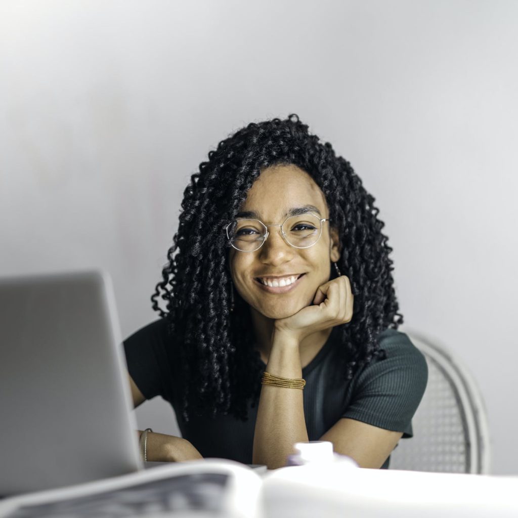 Happy ethnic woman sitting at table with laptop