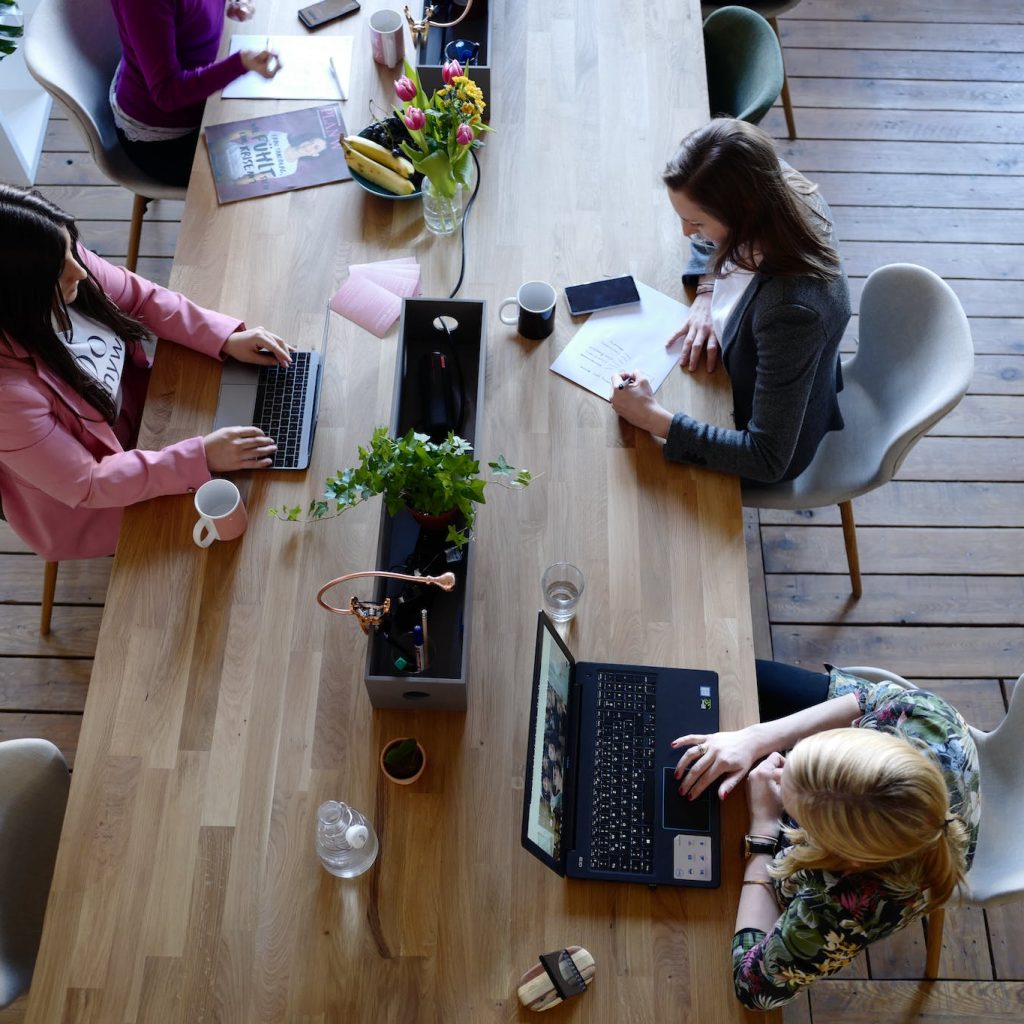 Three Woman Sitting on White Chair in Front of Table